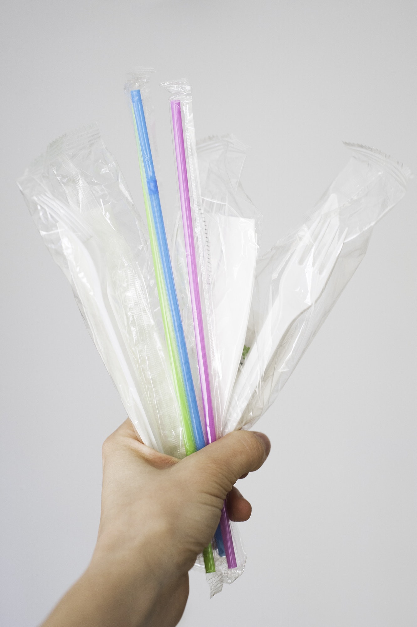 Hand holding compostable plant-based plastic straws and single use cutlery